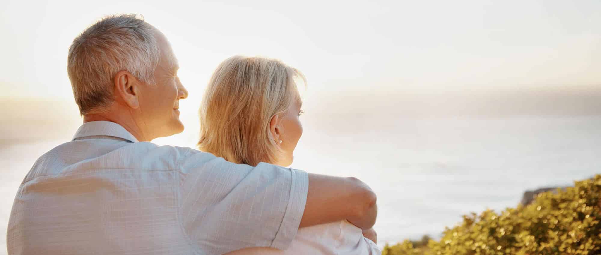 A married couple stands hand in shoulder, peacefully admiring the vast ocean. 