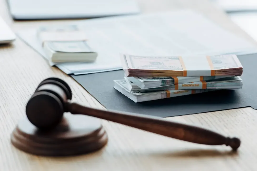A judge's gavel and stacks of money on a desk symbolize justice and finance.