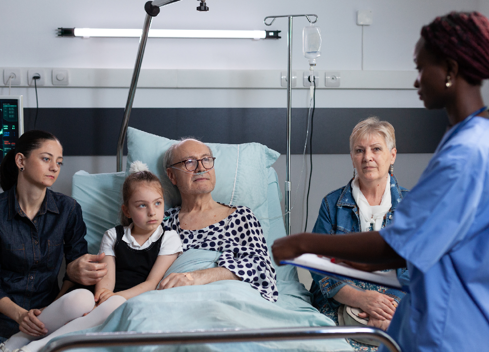 Elderly man in a hospital bed surrounded by his family, representing the impact of asbestos exposure on multiple generations.