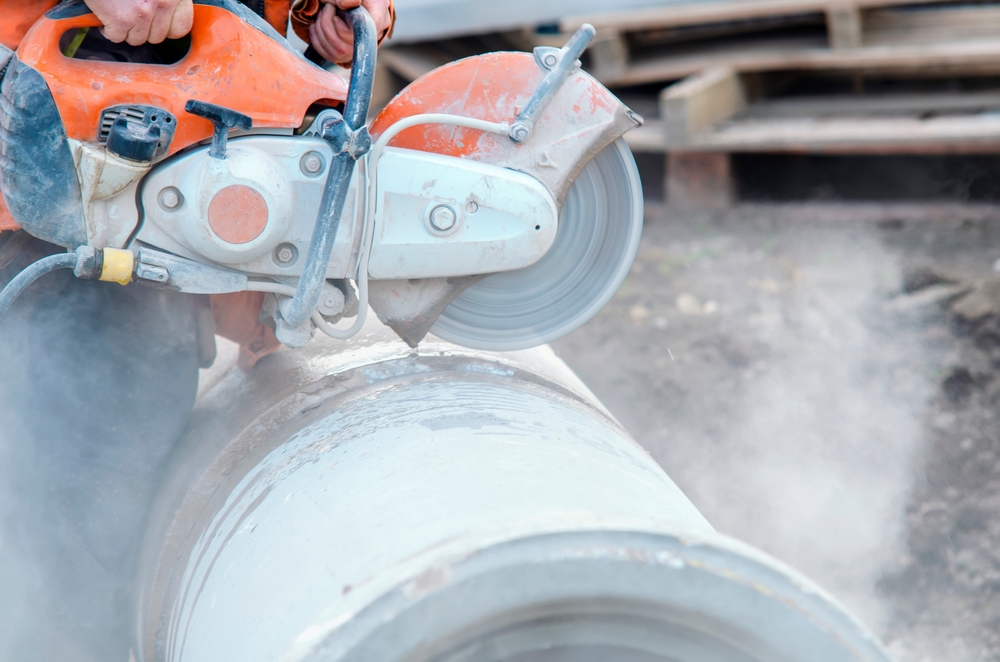 Worker cutting Asbestos-Containing Cement Pipes with a power saw.